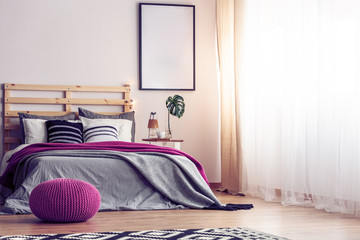 Mockup in black frame on empty wall of bright scandinavian bedroom with comfortable bed with grey bedding, pink blanket and pouf, real photo with copy space lam - obrazy, fototapety, plakaty