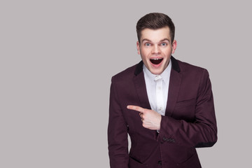 Portrait of surprised handsome young man in violet suit and white shirt, standing, looking at...