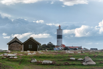 Fototapeta na wymiar Picture of old scandinavian lighthouse and abandoned wooden houses with cloudy sky