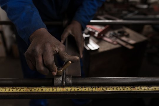 Blacksmith measuring metal rod in workshop