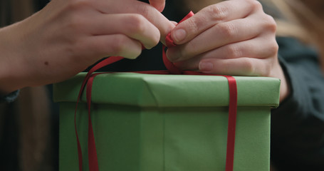 Closeup shot of female hands tying red ribbon bow on green paper gift box
