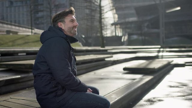 Middle aged man is siiting on a bench in modern urban city in autumn