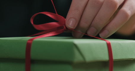 Obraz na płótnie Canvas Macro shot of female hands tying red ribbon bow on green paper gift box