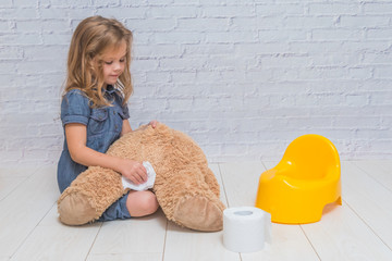 against the background of a white brick wall, the girl sits on a potty with the child, wiping her ass with toilet paper - obrazy, fototapety, plakaty