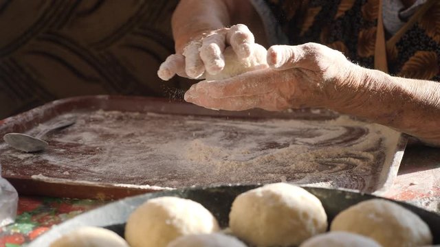 Grandmother's hands make cakes. Wrinkled female hands roll balls of dough. Knead the dough in the home kitchen.
