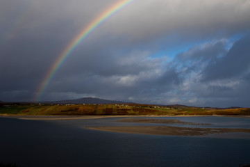 Rural Scottish croft town caught in the sunlight during the morning with stormy clouds and a rainbow. © Paul