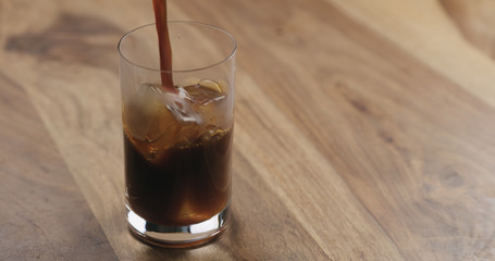 Espresso pour into glass with ice on wood table
