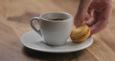 man hand put orange macaron on saucer with coffee cup