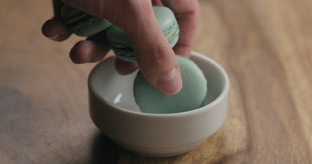 man hand put light blue macarons in white bowl on wood table