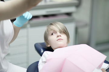 A boy of school age with a stylish haircut is in the dental chair at the reception at the doctor.
