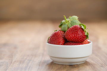 Fresh strawberries in white bowl on wood background with copy space