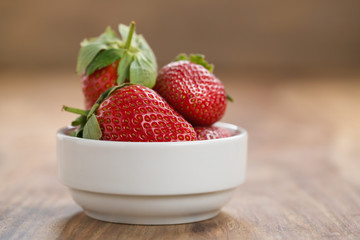 Fresh strawberries in white bowl on wood background with copy space