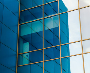 mirrored windows of the facade of an office building with blue panels and yellow window frames with a distorted reflection of the house