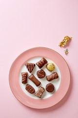 Chocolate pralines selection on a pink plate viewed from above. Various chocolate shapes with golden foil. Top view. Copy space