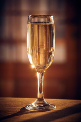 Shot of the champagne glass on a wooden table. Sunlight and bubbles. New year celebration or wedding concept theme
