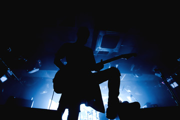 Guitarist silhouette in darkness on a stage in blue back lights playing solo
