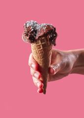 The hand of a man holds a waffle cone with fruit, ice cream decorated with coconut chips on a pink background with copy space.