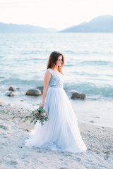 Fototapeta na wymiar Beautiful bride in blue elegant dress holds a bouquet of flowers walking on the shores of Lake Garda. Sirmione, Italy