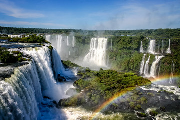 Water cascading over the Iguacu falls with rainbow in foreground in Brazil