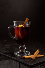 closeup glass of mulled wine with orange and cinnamon on dark black background