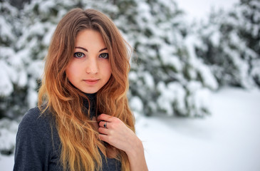 Beautiful young girl posing in the winter in cold forest with pine trees.