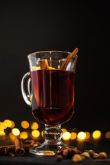 closeup glass of mulled wine with orange and cinnamon on dark black background,  christmas lights, large yellow bokeh, mulled wine set