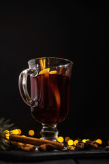 closeup glass of mulled wine with orange and cinnamon on dark black background,  christmas lights, large yellow bokeh, mulled wine set