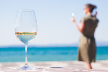 glass of chilled white wine on table over young woman and Garda Lake backgound