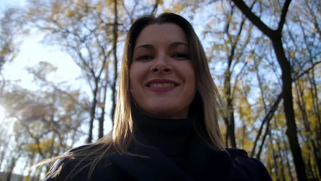 Portrait of a smiling woman circling in the autumn Park slow motion. 4k 60fps. Girl in a coat walking in the autumn city Park. Close up