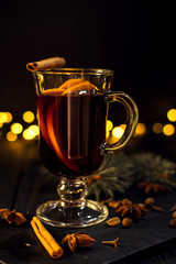 cinnamon lies in a glass, closeup glass of mulled wine with orange and cinnamon on dark black...