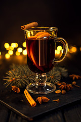 cinnamon lies in a glass, closeup glass of mulled wine with orange and cinnamon on dark black...