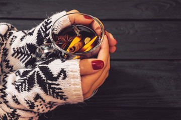 mulled wine in hands of woman on black wooden table, cinnamon sticks and orange, top view,  mulled wine set