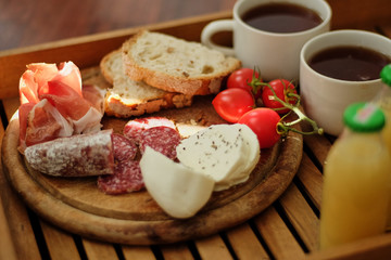 Breakfast in bed. Fresh organic homemade smorrebrod sandwich with cereal dark rye cereal toasts, salami, cherry tomatoes, prosciutto and black coffee mug on a wooden board.