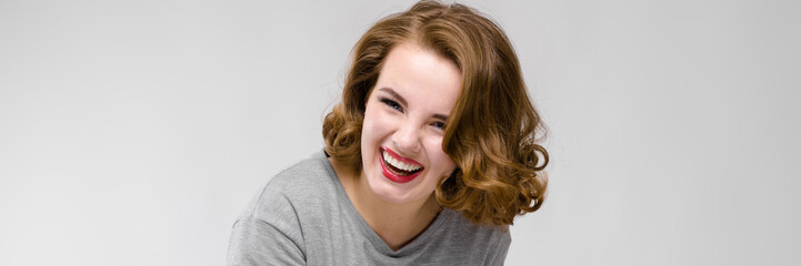 Naklejka premium Charming young girl in a gray T-shirt on a gray background. The girl points with her finger and laughs