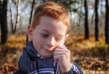 A boy in a plaid scarf around his neck in the autumn forest, blurred background, close-up.