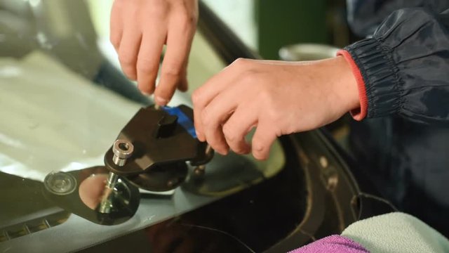Close-up of a man professionally in the workshop engaged in eliminating cracks on the windshield of the car. Vacuum filler job