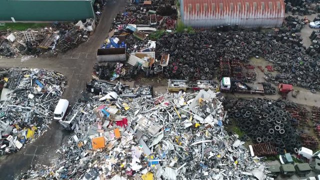 Aerial flight moving backwards over junkyard is the location of a business in dismantling where wrecked or decommissioned vehicles are brought showing pile of recyclable metal and old tires 4k quality