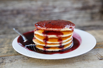 Stack of Pancakes with Blueberry Syrup on a Plate Outside on a Wood Table