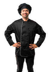 Chef man In black uniform posing with arms at hip and laughing looking to the front on isolated white background