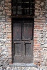 The wooden entrance gate in a house with walls made of rock, stone and brick pieces. Restored wall of ancient Italian architecture