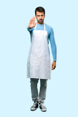 Full body of Man wearing an apron making stop gesture with her hand denying a situation that thinks wrong on blue background