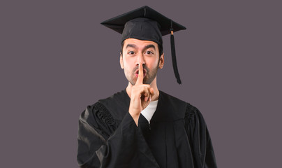 Man on his graduation day University showing a sign of closing mouth and silence gesture putting finger in mouth on violet background