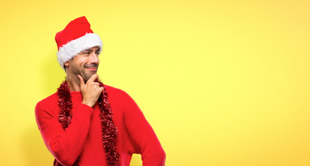 Man with red clothes celebrating the Christmas holidays looking to the side with the hand on the chin on yellow background