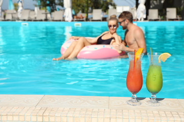 Refreshing cocktails and young couple in swimming pool on background