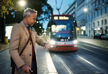 Mature businessman with suitcase waiting for a tram in the evening.