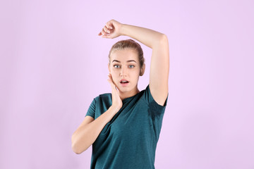 Young woman with sweat stain on her clothes against color background. Using deodorant
