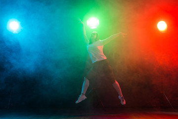 Obraz premium Dancing, sport, jazz funk and people concept - young woman jump in the darkness under colourful light