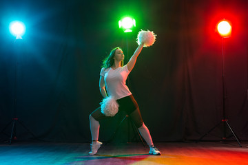 Cheerleading young woman dancing with pom-poms on colourful background © satura_