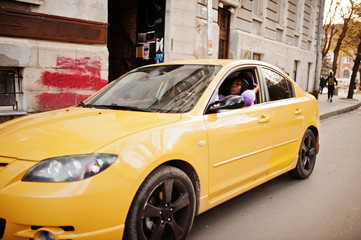 Fototapeta na wymiar African american woman at violet dress and cap posed at yellow car.