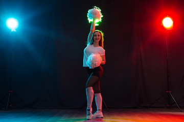 Cheerleading young woman dancing with pom-poms on colourful background